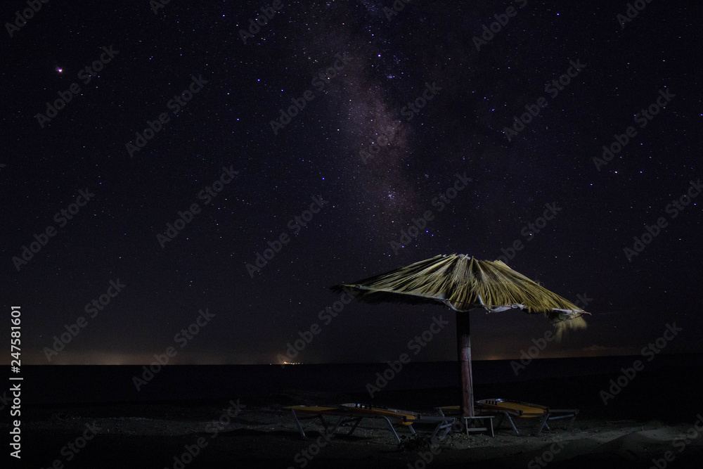 straw umbrella with sits on the spotlight night with milky way in the sky