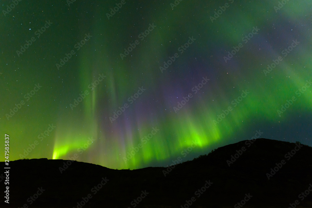 Northern, aurora borealis in the sky above the hills. Violet and green. Color.