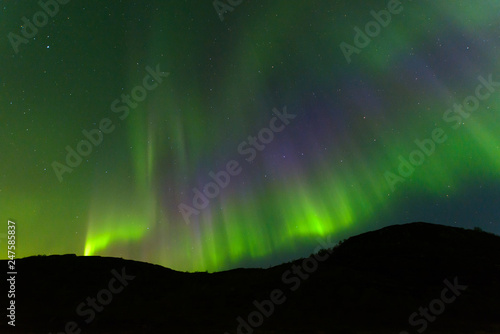 Northern  aurora borealis in the sky above the hills. Violet and green. Color.