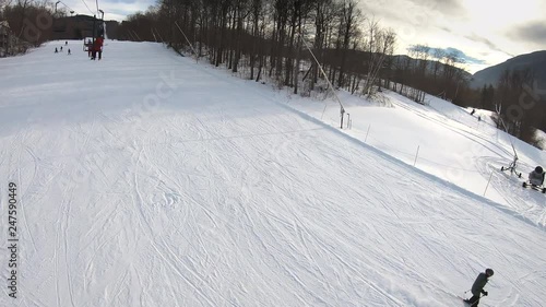 Skiers going down the slope and making turns. People having fun skiing on a groomed trail and making turns. Beautiful Vermont winter vacation. Aerial view form the chair lift. Wide shot.