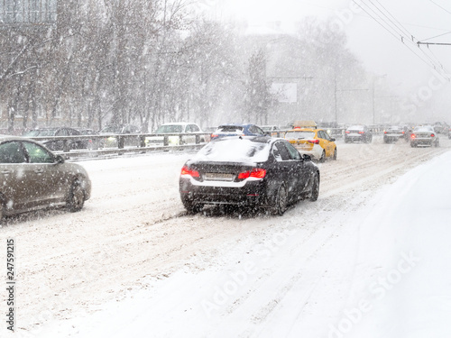 cars drive at slippery street in snow blizzard