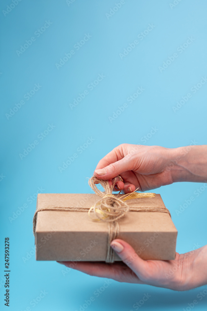 Hands holding gift box Packed in Kraft paper on blue background. Holiday card for Valentine's day and women's day