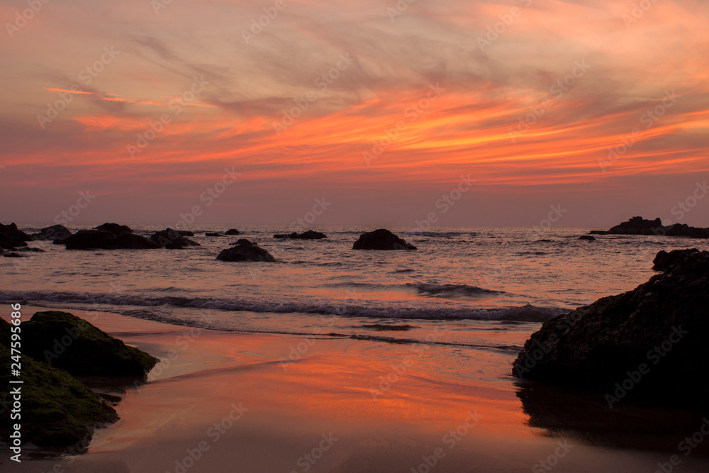 sandy beach on the background of rocks in the sea and bright orange pink purple sunset sky