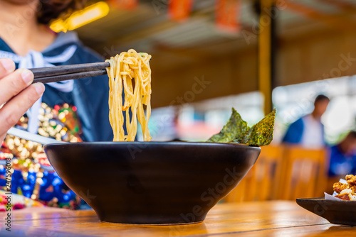 Woman eating a spicy ramen Japanese noodle soup in a black color ramen bowl.