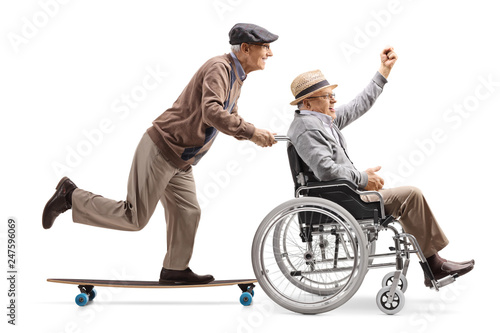 Elderly man on a longboard pushing a man with raised hand in a wheelchair