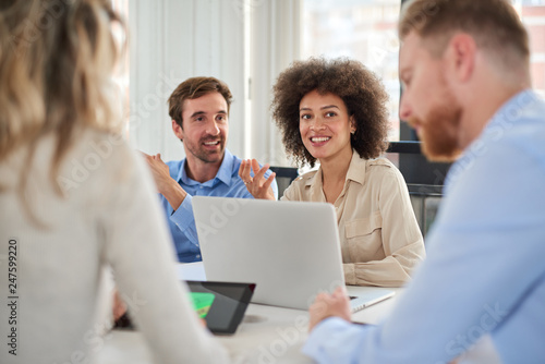 Small group of business people sitting at table and having meeting. Multi cultural group. Selective focus on mixed race woman.