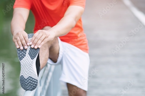 young man runner stretching for warming up before running or before a morning workout working out jogging in the park. track and field athlete exercise. Fitness and sport healthy lifestyle concept.