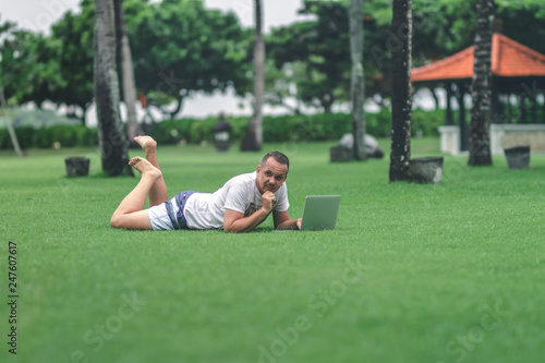 Young man in the green tropical park working online with laptop. Freelancer man on Bali island concept.