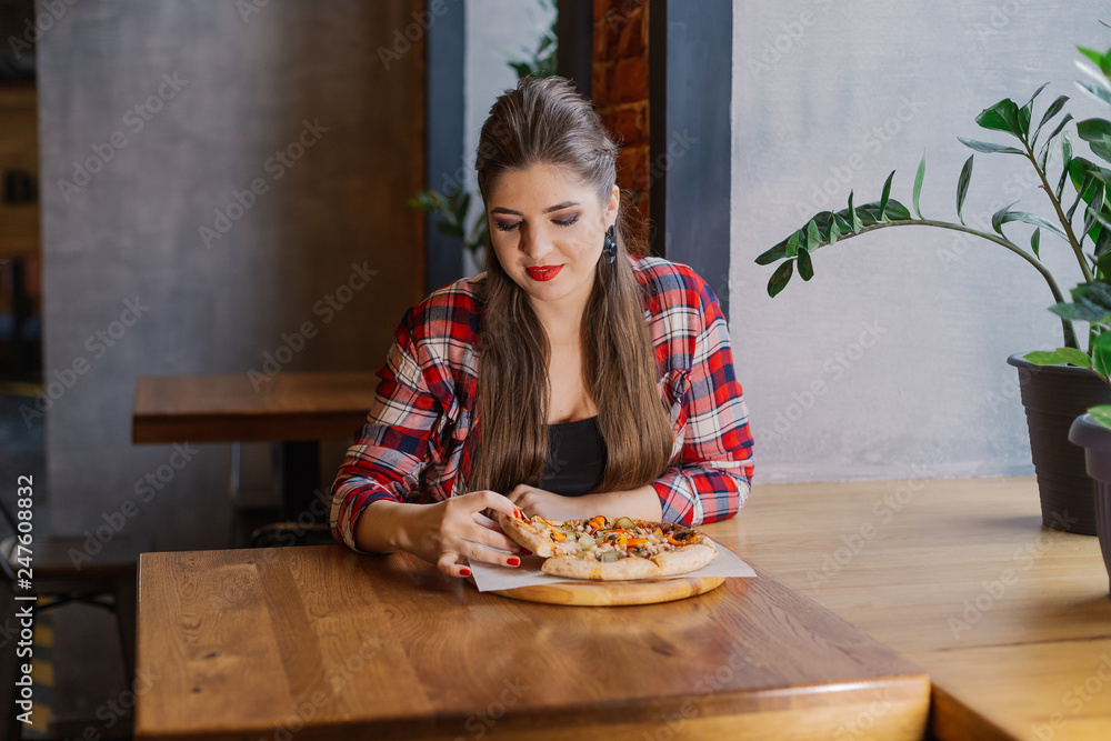 Beautiful and sexy girl sitting by the window in a cafe and holding a pizza. Beautiful and sexy girl sitting by the window in a cafe and holding a pizza.