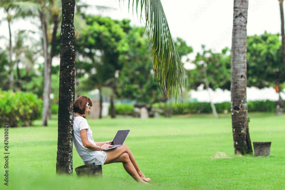 Woman online shopping concept. Woman in the green park with modern laptop. Bali island.