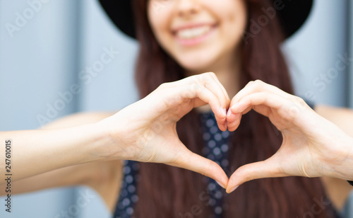 Closeup shot of cheerful girl with long hair making heart shape with her fingers. Space for text