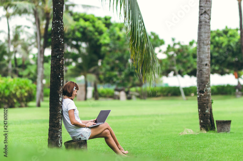Woman online shopping concept. Woman in the green park with modern laptop. Bali island.