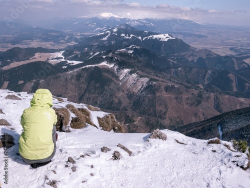 Tourist sitting at the edge of rock looking out into winter countryside on large mountain © Kamil