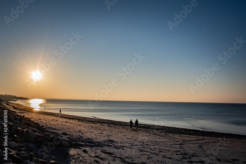 Photos Sun setting over ocean on a windless day with people walking on the beach in the distance