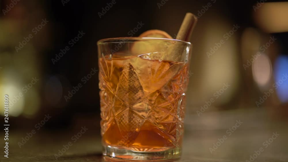 Alcohol shot with orange and ice is at the table close up. Bartender puts cinnamon in the glass Alcohol shot with orange and ice is at the table close up. Bartender puts cinnamon in the glass