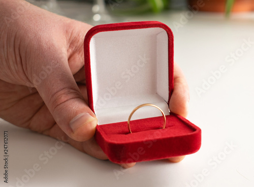 Wedding ring red box surrounded by rose petals. An offer of marriage. Box with a ring in the hands of a man on a blurred background