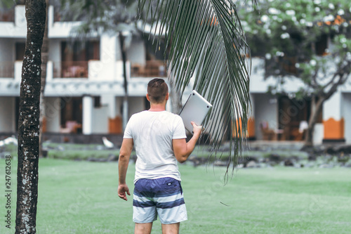 Young freelancer man with laptop in the green tropical park of Bali island.