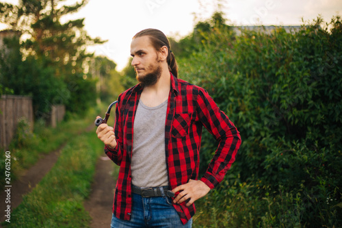 A rustic man with a beard and a red shirt in a cage. A young hipster guy with a pipe in his hand.