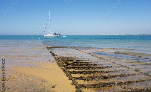 Abandoned batea in Formosa  estuary (mollusc farm). Sailboat in the beach of Farol Island, Algarve, Portugal