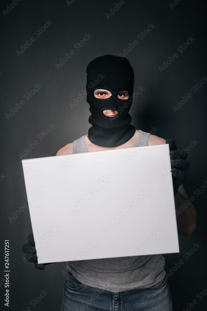 A man in a black mask holds a white sheet. A guy in a balaclava and wearing gloves holds a white empty square. A man on a gray background holds a canvas. A man in a black mask holds a white sheet. A guy in a balaclava and wearing gloves holds a white empty square. A man on a gray background holds a canvas.
