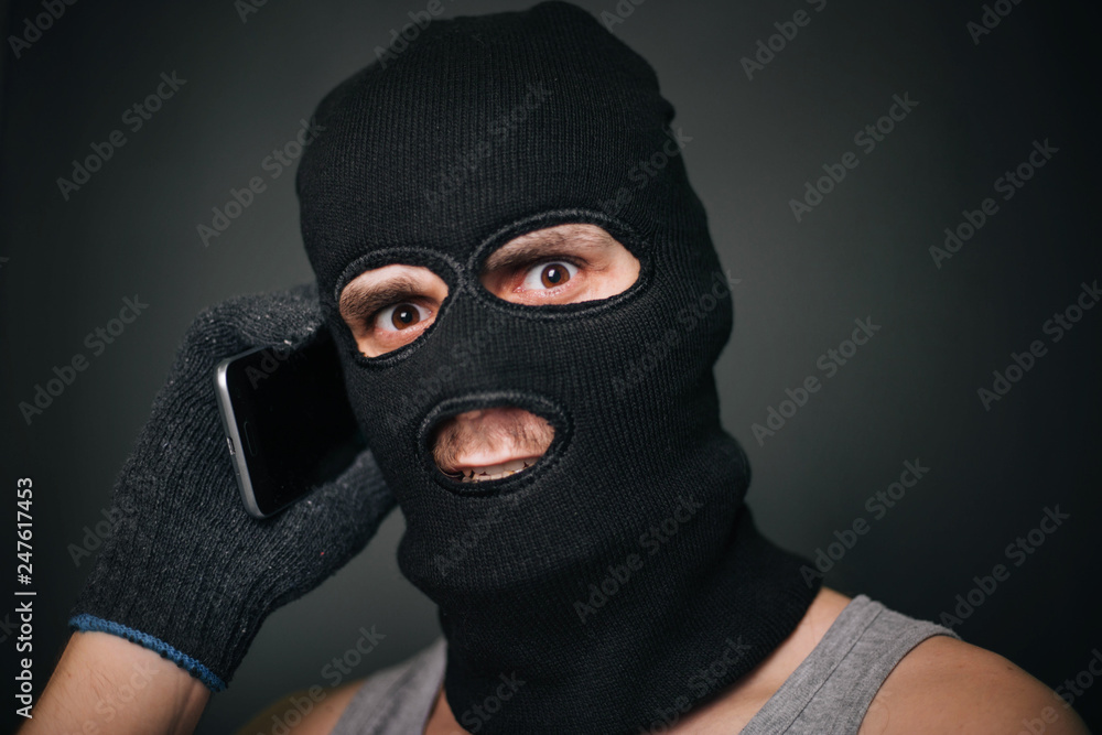 The criminal in a black mask with a smartphone. a guy in a balaclava and a cell phone. The criminal is negotiating The criminal in a black mask with a smartphone. a guy in a balaclava and a cell phone. The criminal is negotiating