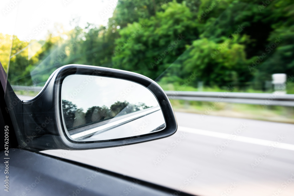 Car rear-view mirror on the motorway in summer in Germany with green trees in the background