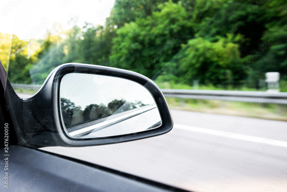 Car rear-view mirror on the motorway in summer in Germany with green trees in the background Car rear-view mirror on the motorway in summer in Germany with green trees in the background