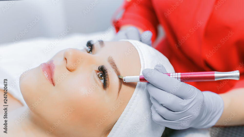 Naklejka premium Beautiful young girl with long eyelashes tweezing her eyebrows in a beauty salon. Eyebrow Correction. Beauty Concept. Permanent Makeup. Microblading brow. Beautician Doing brows Tattooing.