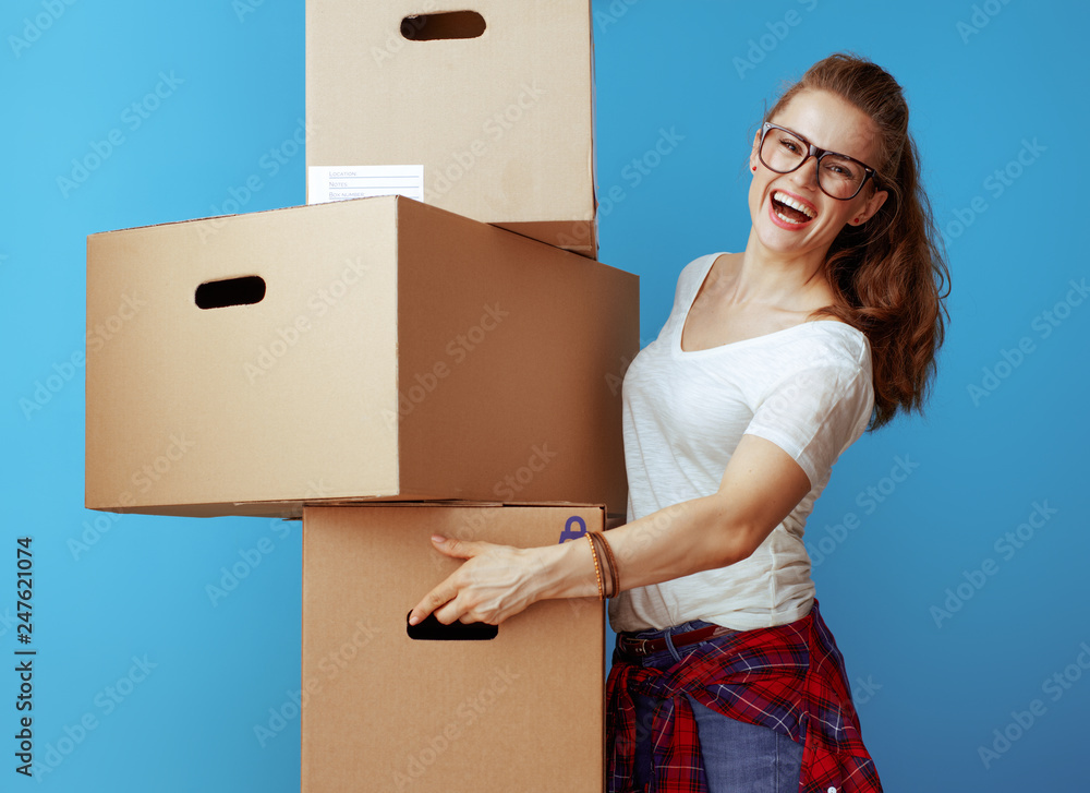 smiling modern woman holding pile of cardboard boxes on blue smiling modern woman holding pile of cardboard boxes on blue