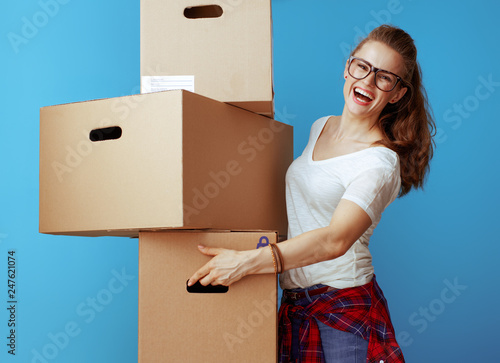 smiling modern woman holding pile of cardboard boxes on blue