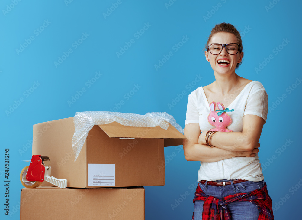 smiling young woman near cardboard box hugging old toy on blue smiling young woman near cardboard box hugging old toy on blue