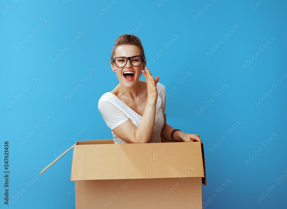 happy woman in cardboard box telling exciting news on blue happy woman in cardboard box telling exciting news on blue