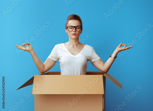 relaxed modern woman doing yoga in cardboard box on blue