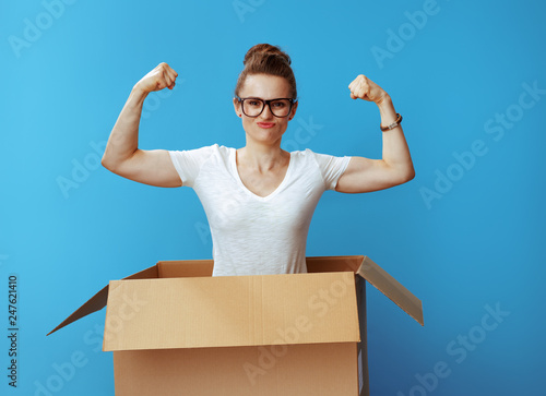 powerful young woman showing biceps in cardboard box on blue