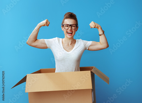 happy young woman showing biceps in cardboard box on blue