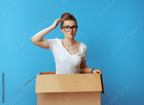 pensive modern woman in white t-shirt in cardboard box on blue