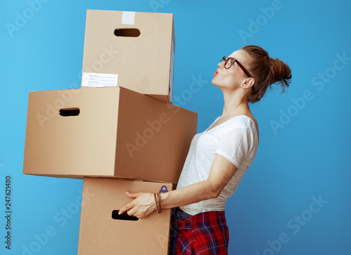 woman holding pile of cardboard boxes and looking up on blue