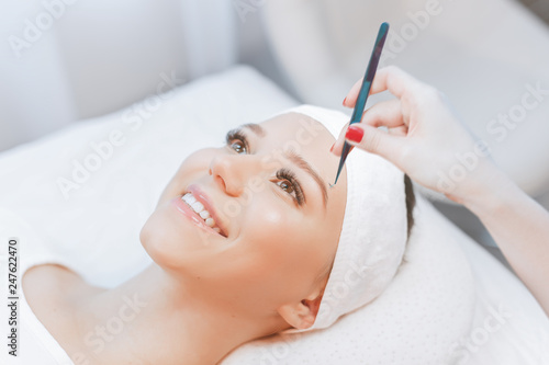 Eyelash Extension Procedure. Close up view of beautiful Woman with Long Eyelashes. Stylist holding tweezers, tongs and making lengthening lashes for girl in a beauty salon. Beauty Concept.