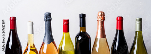 Tops from different kinds new bottles of champagne, white, red wine on light background