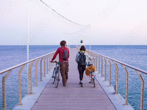 couple with bicycles strolling on a maritime pathway over the sea a sunny day photo