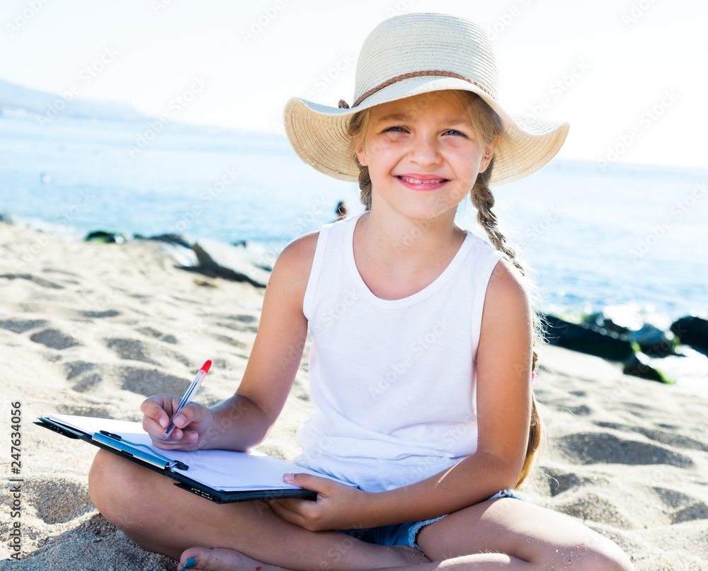 child girl in hat writes draws dreams with sand on seashore