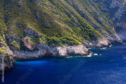 rocky sea coast of the Greek island of Zakynthos with green vegetation and dark blue water on the bright sun