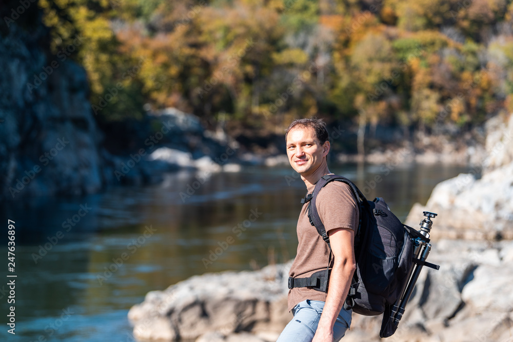 Young photographer man happy on trail path road during autumn Potomac river in Great Falls, Maryland with colorful foliage and backpack tripod