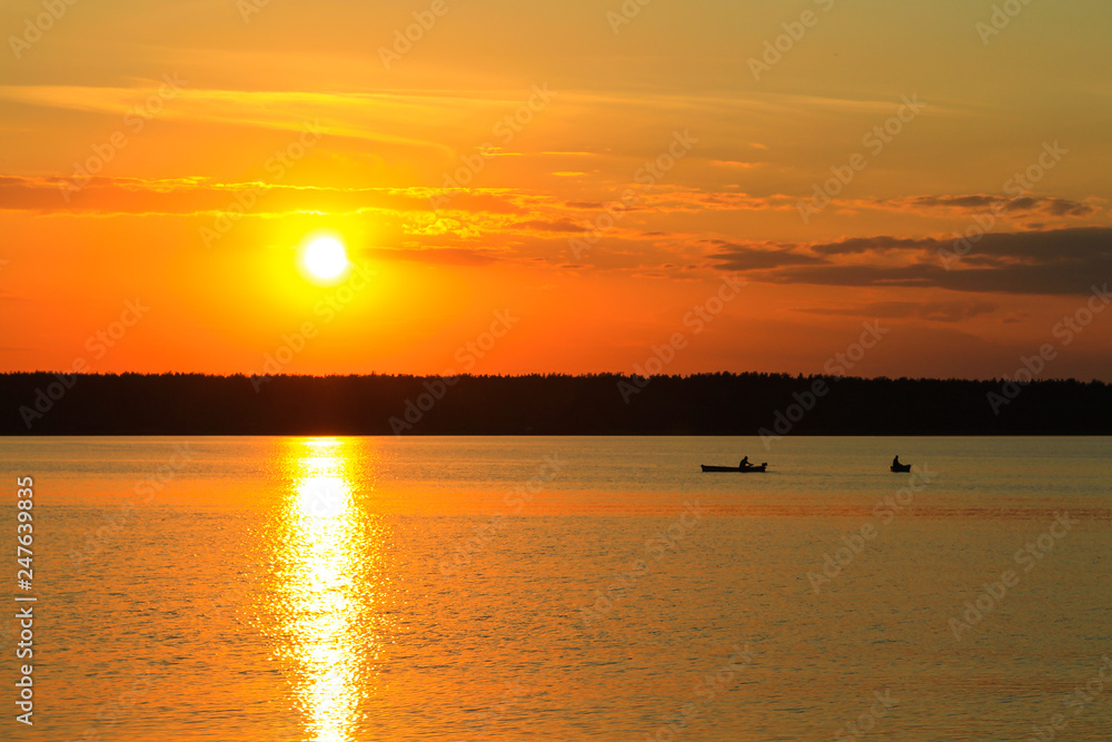 Fishermen float on a lake at sunset