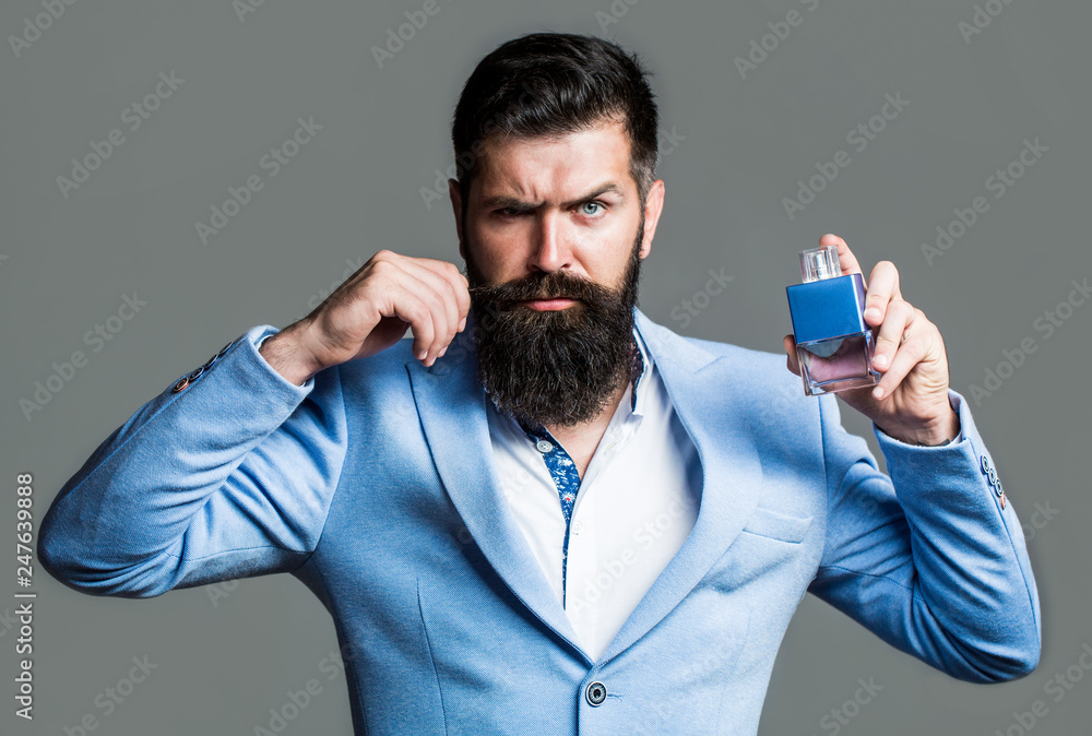Bearded man holding up bottle of perfume. Fashion cologne bottle