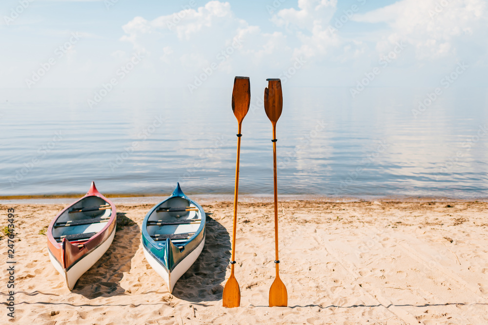 Canoe on beach in sunny summer day on blurred sea with clouds background. Kayak with wooden paddles on coast of mediterranean sea. Summer adventure. Travel, tourism, vacation concept. Boat rent. Canoe on beach in sunny summer day on blurred sea with clouds background. Kayak with wooden paddles on coast of mediterranean sea. Summer adventure. Travel, tourism, vacation concept. Boat rent.