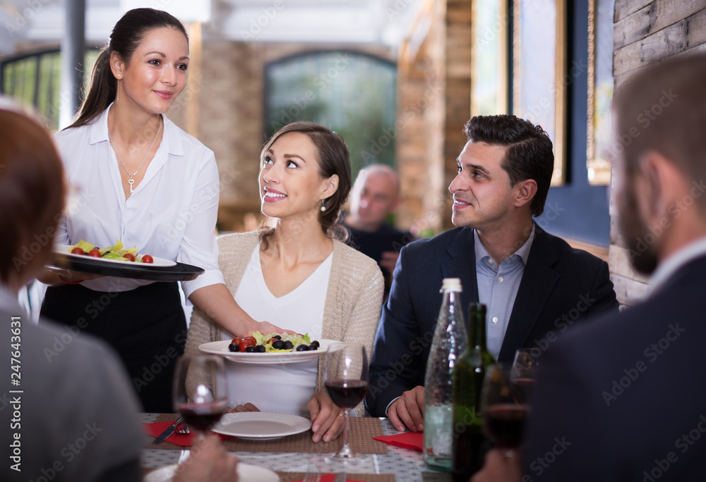 Waitress with dishes serving male and female