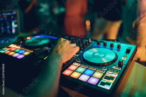 DJ plays live set and mixing music on turntable console at stage in the night club. Disc Jokey Hands on a sound mixer station at club party. DJ mixer controller panel for playing music and partying.
