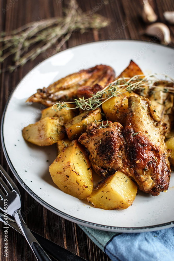 Baked chicken wings with potatoes and garlic on a rustic background Baked chicken wings with potatoes and garlic on a rustic background