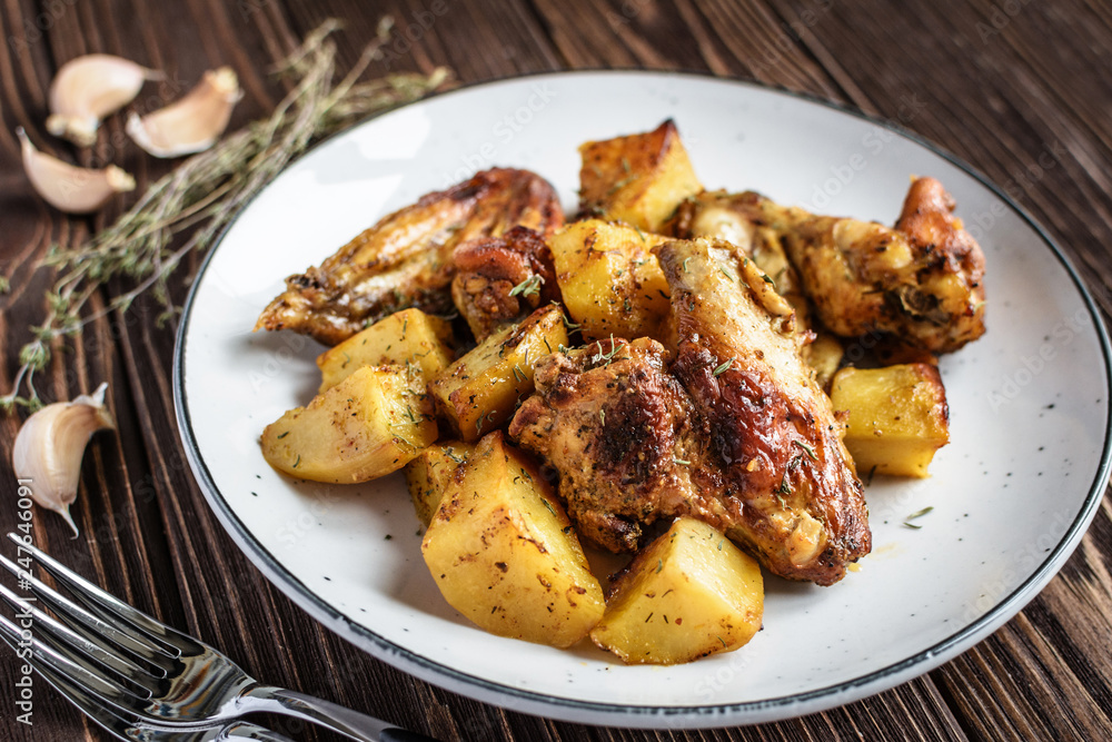 Baked chicken wings with potatoes and garlic on a rustic background Baked chicken wings with potatoes and garlic on a rustic background